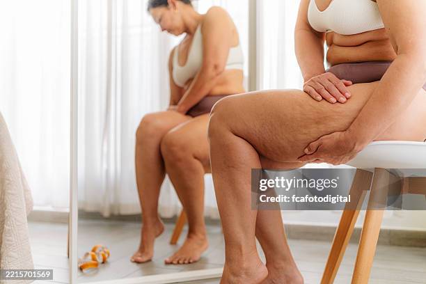 übergewichtige frau mit cellulite in den dicken oberschenkeln sitzt vor dem spiegel - fette frau stock-fotos und bilder