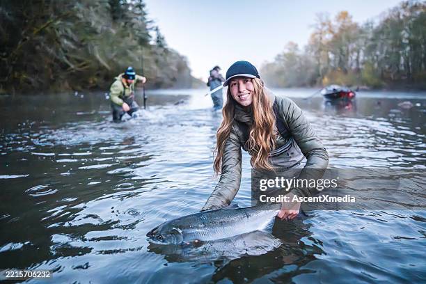 porträt einer jungen frau, die lachs im fluss hält - fischereiindustrie stock-fotos und bilder