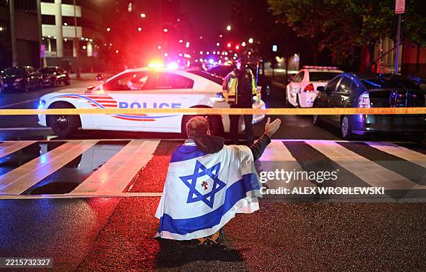 Man draped in the Israeli flag, bearing a cross and the name "Jesus" at its center, gestures as Metropolitan Police officers secure the area outside...