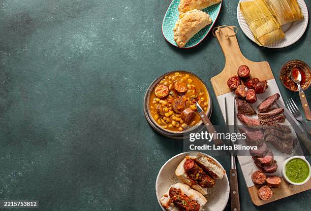 selection of argentinian festive food. table for independence and revolution day with asado, locro, empanadas, corn tamales and choripan - chimichurri stock pictures, royalty-free photos & images