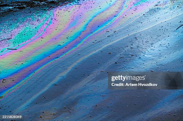 iridescent oil spill creating a colorful abstract pattern on wet asphalt - ölpest stock-fotos und bilder