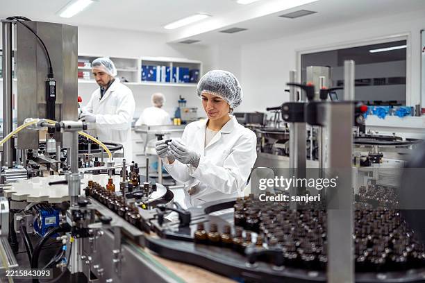 mid adult female lab worker in white coat packaging products in a modern laboratory - farmaceutische-fabriek stockfoto's en -beelden