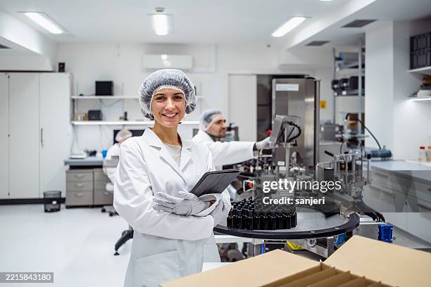 trabajadora de laboratorio femenina adulta media sonriente en tableta de sostenimiento de bata blanca en laboratorio moderno - fábrica farmacéutica fotografías e imágenes de stock