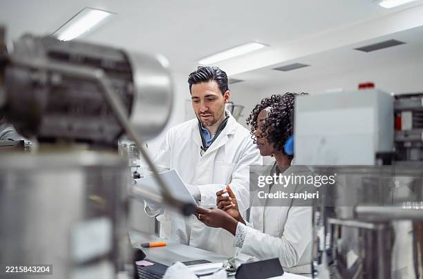 multi-ethnic pharmaceutical scientists review data in modern laboratory setting - product test stockfoto's en -beelden