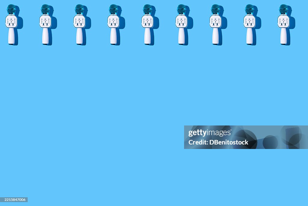 Pattern of metallic blue microphones with speakers, for karaoke, on top, on a blue background. Music, podcast, singer, concert, presenter, and show.