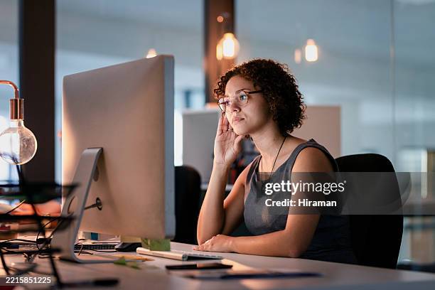 femme d’affaires concentrée travaillant tard dans un bureau moderne, assise à son bureau - regarder fixement photos et images de collection