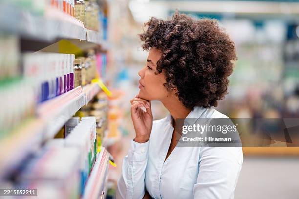 woman in pharmacy browsing medicine shelf contemplatively - microbiome stock pictures, royalty-free photos & images