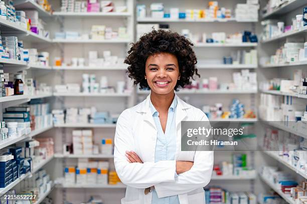 smiling female pharmacist in lab coat standing in pharmacy with medicine shelves - apotheker stockfoto's en -beelden