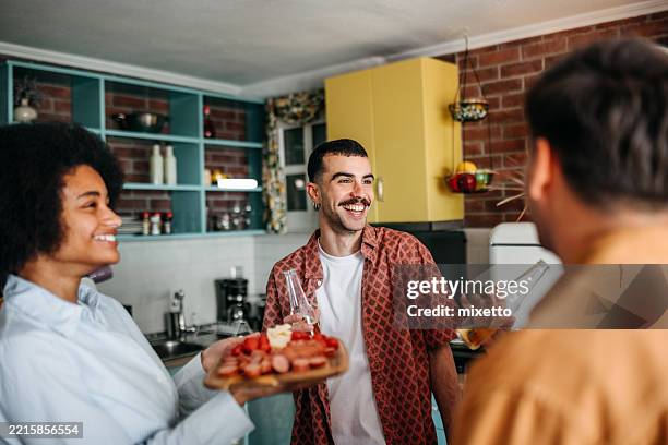 friends gathered around wooden board with food and drinks at home party - generosity stock pictures, royalty-free photos & images