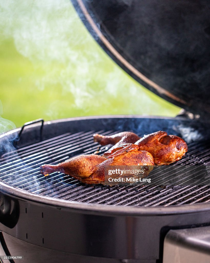 Two seasoned chicken halves smoking on a charcoal grill.