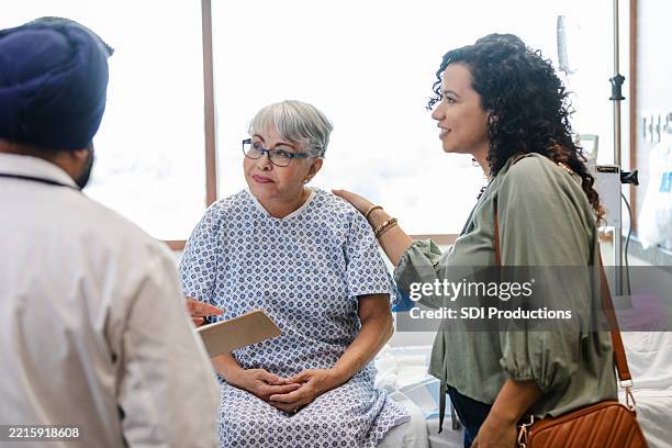 supportive daughter with mother at doctor's office - examination gown stock pictures, royalty-free photos & images