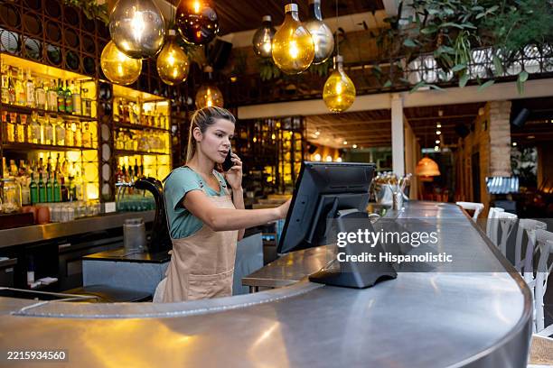 waitress talking on the phone taking a reservation at a restaurant - caixa registadora imagens e fotografias de stock