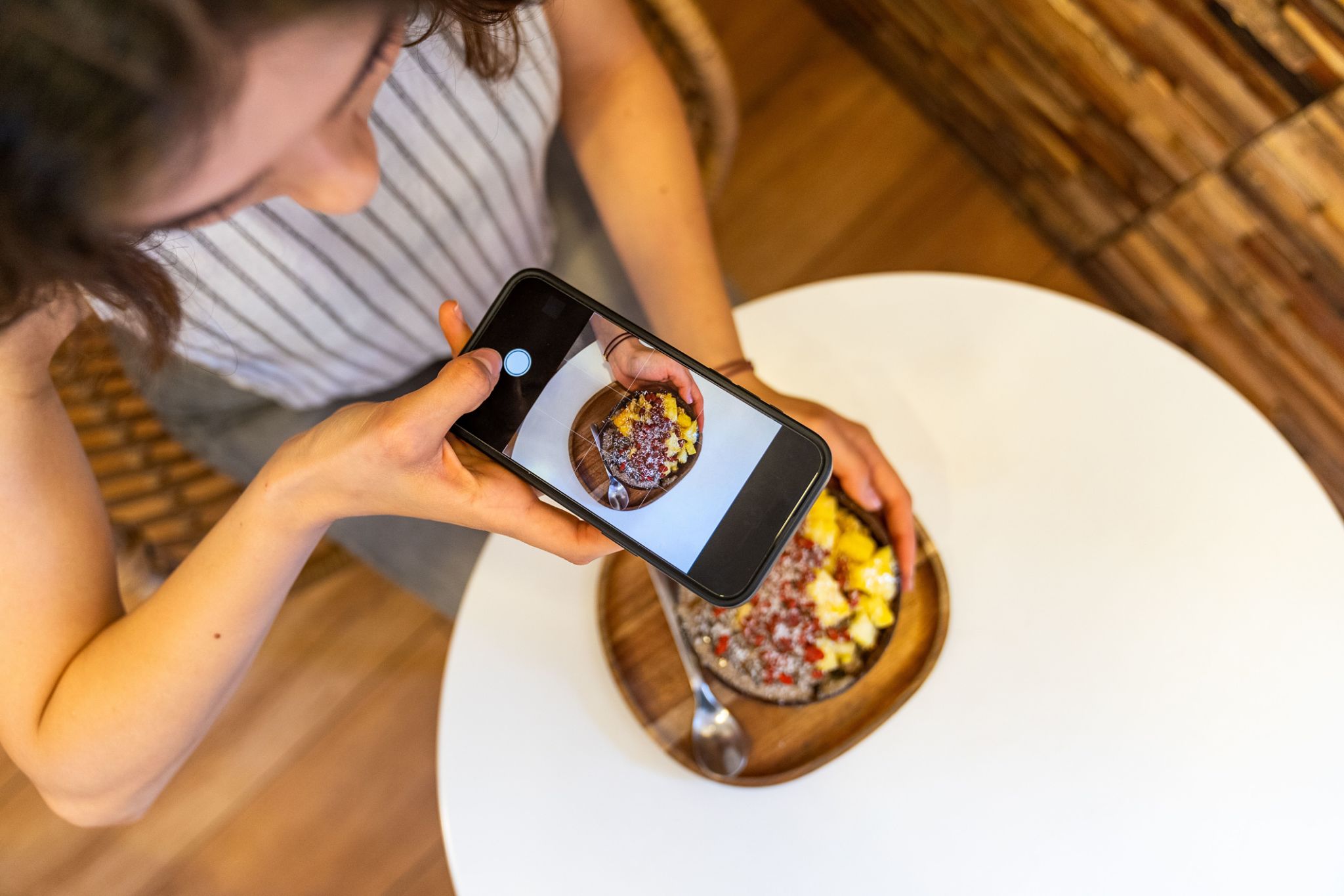 Woman taking photo of acai bowl with smartphone in cafe. Woman taking photo of acai bowl with smartphone in cafe.