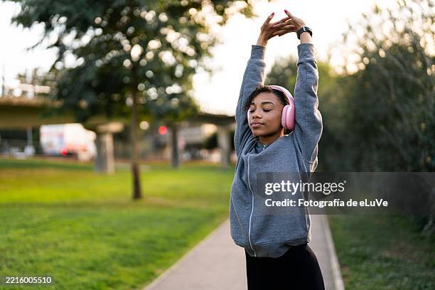 young woman stretching in a park while listening to music - corredora de footing fotografías e imágenes de stock