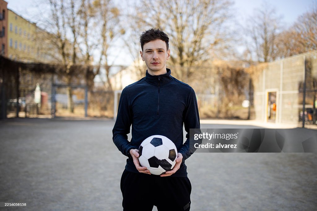 Man holding a soccer ball standing in urban sports court