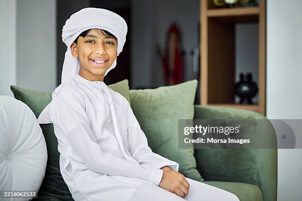 smiling middle eastern boy sitting on sofa - arab boy stock pictures, royalty-free photos & images