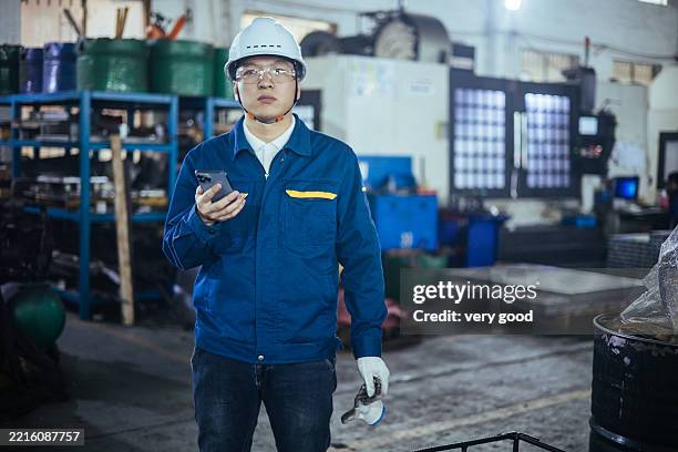 asian male engineer wokring with smart phone in factory - wokring out stock pictures, royalty-free photos & images