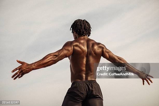 rückansicht eines hemdlosen, athletischen mannes, der seine arme im freien hebt - menschlicher muskel stock-fotos und bilder