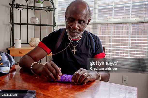 anciano afroamericano de setenta años con un tubo de oxígeno clasificando recetas en la mesa de la cocina de su casa - tubo de oxígeno fotografías e imágenes de stock