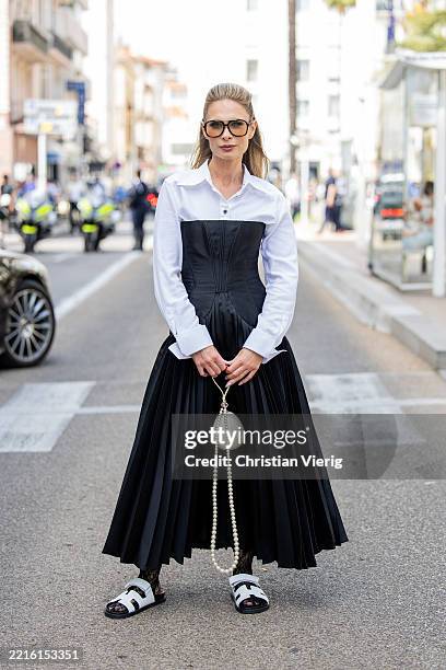 Iryna Thater wears white bag, button shirt, black off shoulder dress Araftu Couture, white sandals during day eight of the 78th Cannes Film Festival...