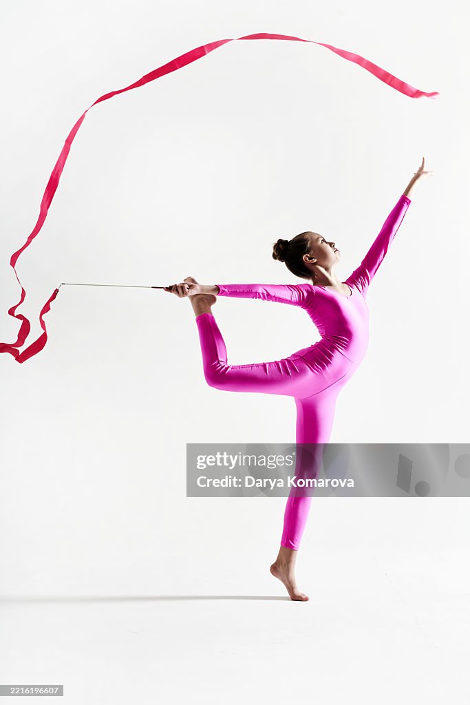 A gymnast girl with a gymnastic ribbon in a pink jumpsuit does a gymnastic exercise.