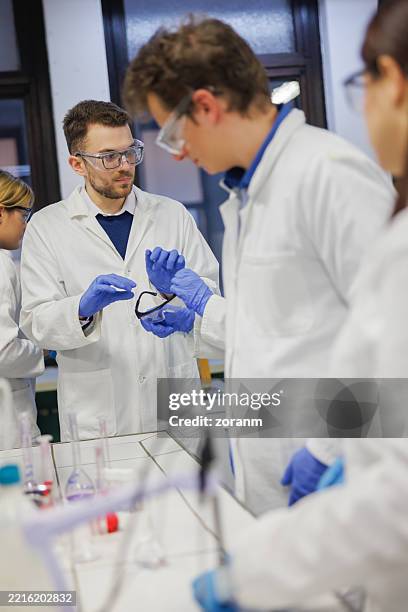 group of students in lab coats, gloves and protective eyewear attending practical class in laboratory - scientific research stock pictures, royalty-free photos & images