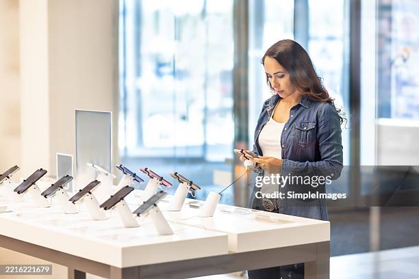 a pretty brunette is trying out a new smartphone in a phone operator's store. she is getting to know the new model. - electronics store stock pictures, royalty-free photos & images