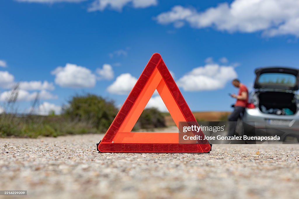 Warning triangle on a country road with broken car and driver