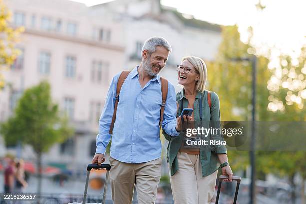 senior couple exploring a city with suitcases, smiling and enjoying their journey - travel insurance stock pictures, royalty-free photos & images
