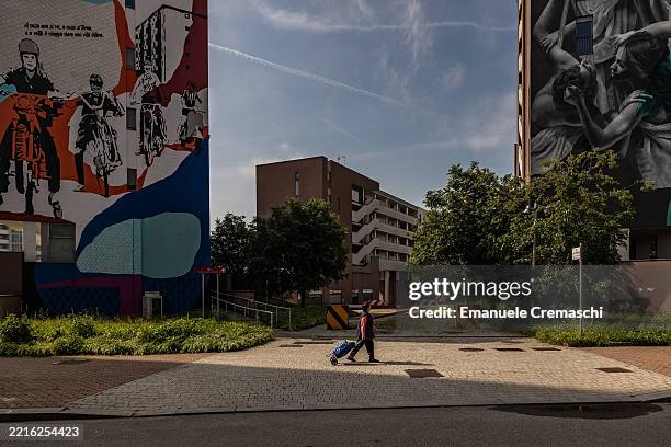 Woman pulls a trolley as she walks past the murals “Il viaggio” by Spanish artist Andrea Michaelsson and “Atlas” by Dutch artist Judith De Leeuw ,...