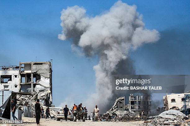 People move past destroyed buildings as smoke billows following an Israeli strike in Jabalia, in the northern Gaza Strip on May 25, 2025. Rescuers in...