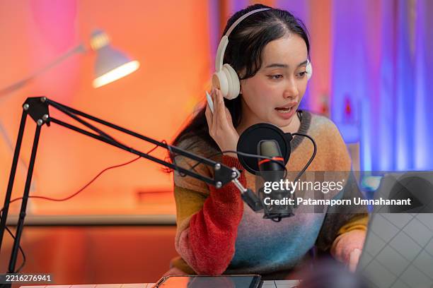 smiling woman wears headphones and talks into a microphone in a professional recording studio. engaging with listeners at home through audio broadcasting, podcasting, and modern communication technology. confidence and creativity in action. - vlogger stockfoto's en -beelden