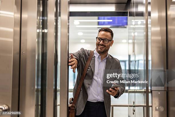 businessman holding elevator door open for someone - lift stockfoto's en -beelden