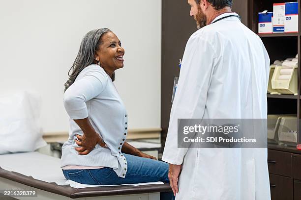 doctor and patient discussing back pain in medical office - heup stockfoto's en -beelden