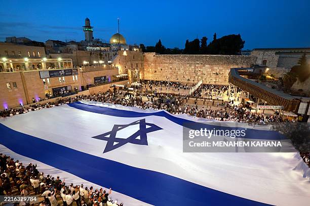 People unfurl a giant Israeli flag at the Western Wall Plaza in the old city of Jerusalem on May 25 on the eve of Jerusalem Day, which commemorates...
