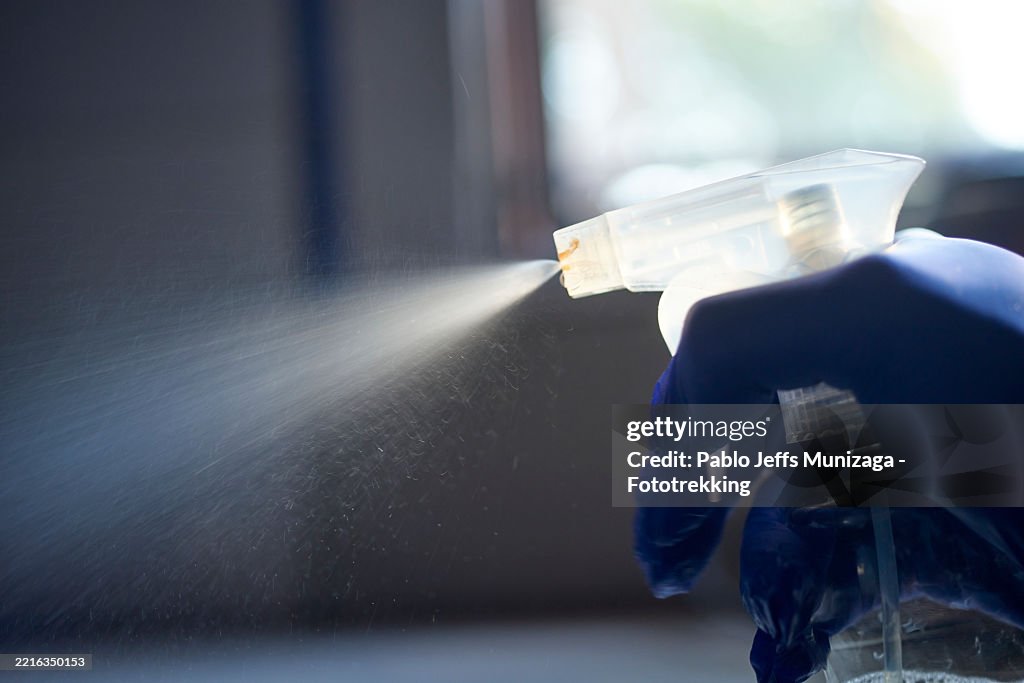 Hand in protective glove spraying sanitizing solution, disinfecting surface during thorough cleaning process, eliminating bacteria and maintaining hygienic workspace
