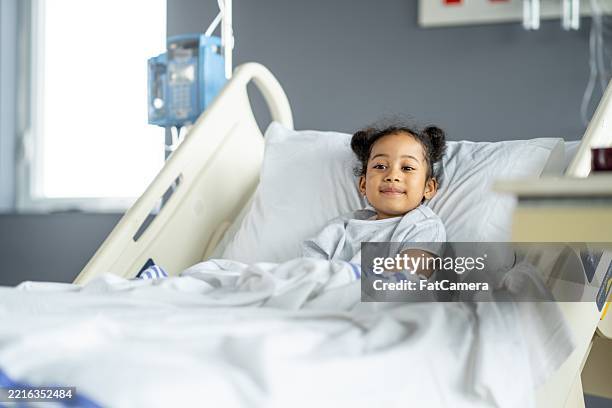niño sonriente descansando cómodamente en una cama de hospital brillante - hospital infantil fotografías e imágenes de stock