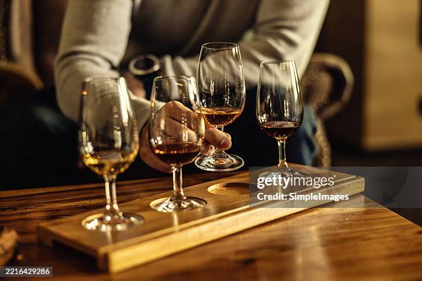 a view of a tasting set of whiskey, rum, cognac or brandy. a man's hand selects a glass of rum from the tasting set. - rum foto e immagini stock