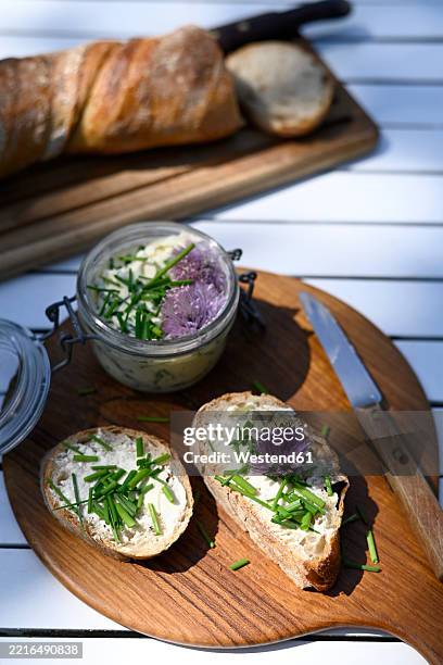 sliced bread with butter and chives spread, served on a wooden board with a knife, outdoors in summer - cebolinho imagens e fotografias de stock