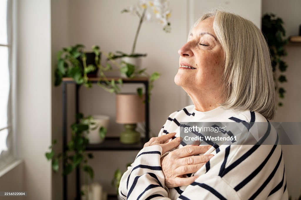 Elderly woman meditating peacefully at home with eyes closed