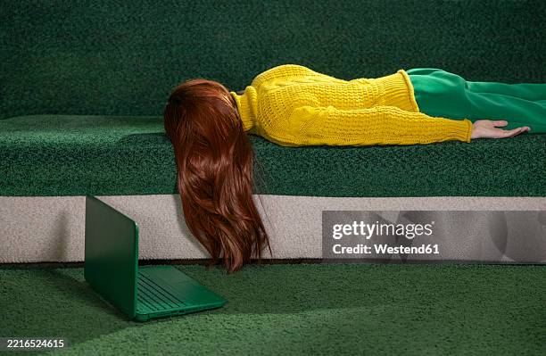 red-haired woman lying on a couch at home with a laptop, appearing tired and resting - burnout imagens e fotografias de stock