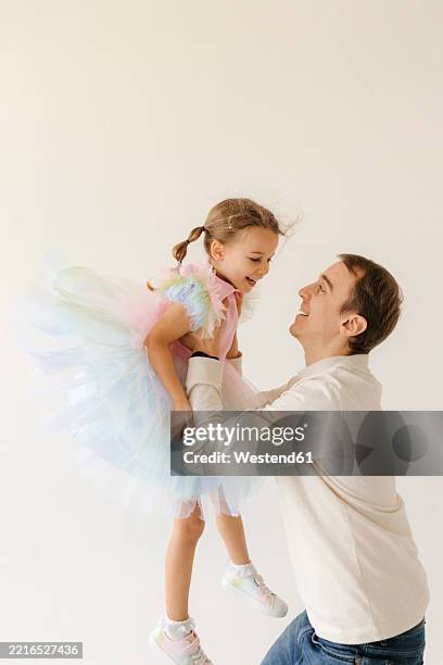 father joyfully lifting daughter in tutu indoors - family excitement stock pictures, royalty-free photos & images