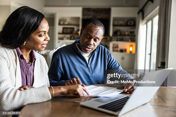 husband and wife looking over bills and using laptop in domestic kitchen - presupuesto fotografías e imágenes de stock