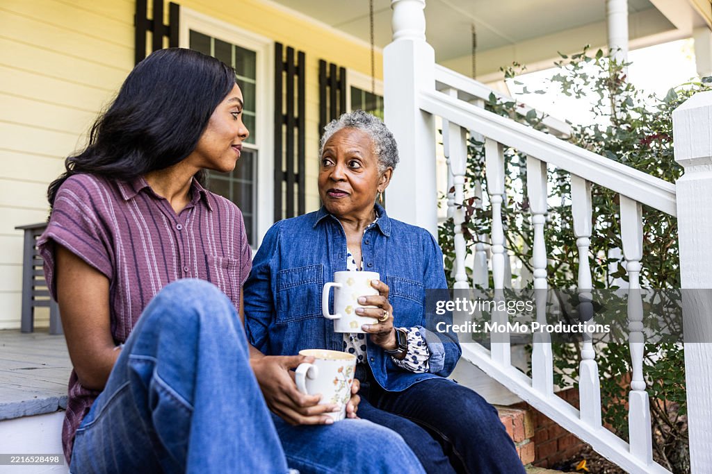 Senior woman and adult daughter having coffee on front porch of rural farm home
