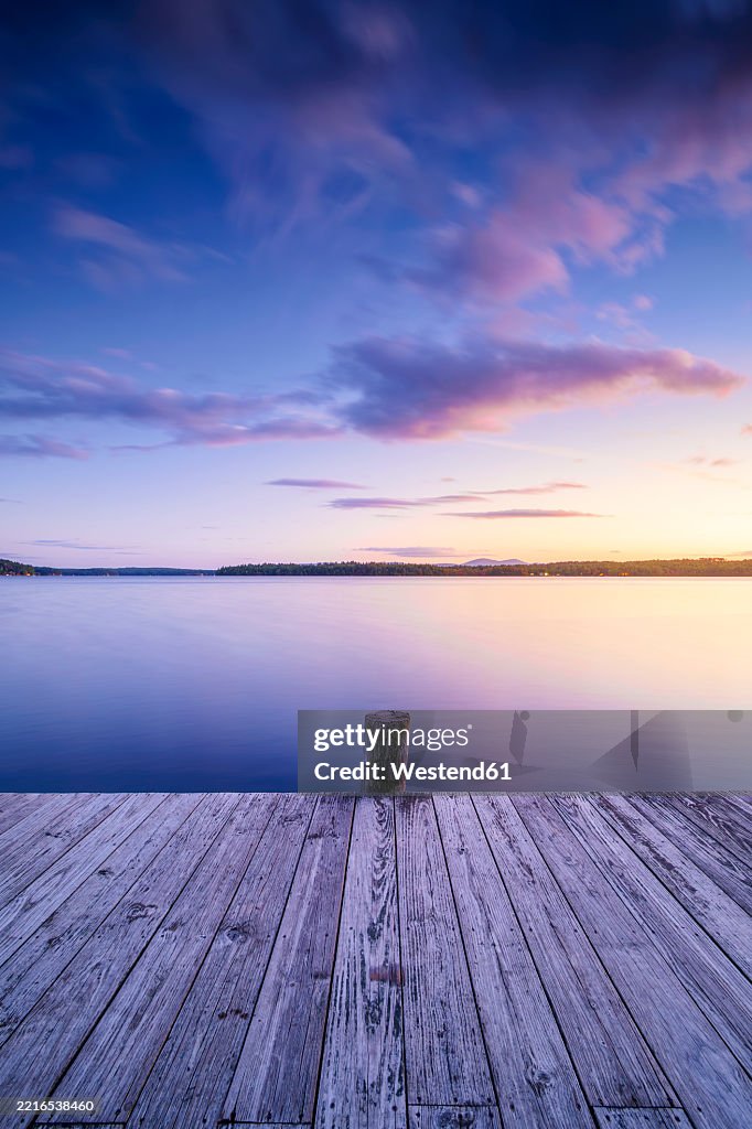 Serene lakeside view at Lake Winnepesaukee during blue hour with a wooden pier and colorful sky