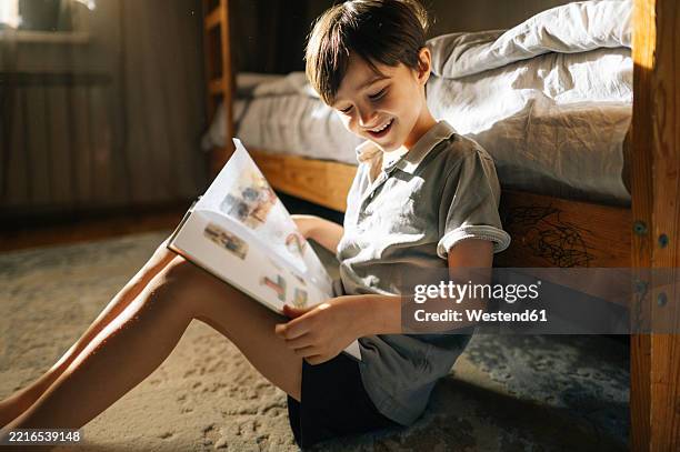 boy reading a book at home in a sunlit bedroom - regarder vers le bas photos et images de collection