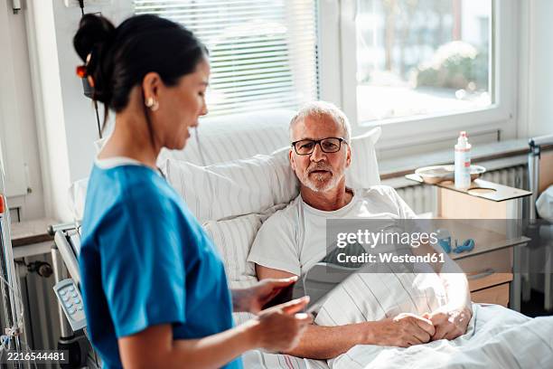 nurse providing care and advice to a patient in a hospital room - rapporto medico paziente foto e immagini stock