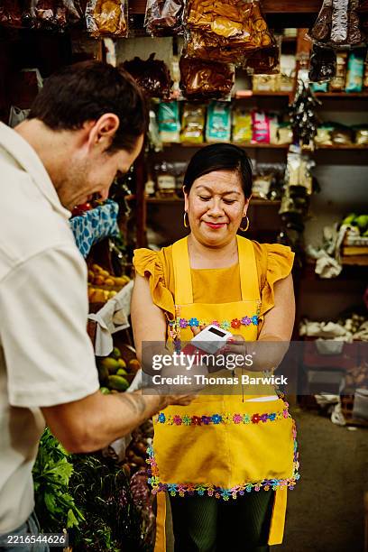 medium wide shot man buying goods with credit card from shop owner - voyage expérientiel photos et images de collection