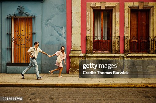Wide shot tourist couple running through the streets of old Oaxaca Wide shot tourist couple running through the streets of old Oaxaca