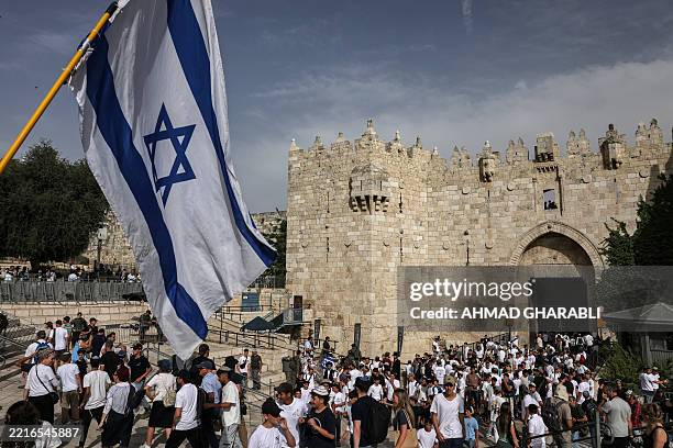 Right-wing activist waves an Israeli flag as others gather outside the Damascus Gate of the walled Old City of Jerusalem on May 26 during a flag...